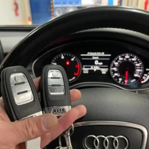 Two Audi remote keys held in front of the steering wheel